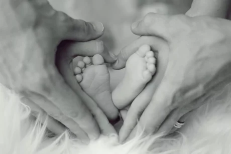 A couple holding their hands around a baby's feet in a heart shape