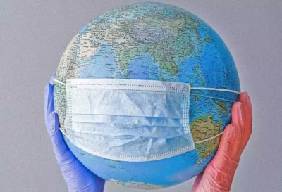 A globe being held aloft by disposable-gloved hands with a face mask around it