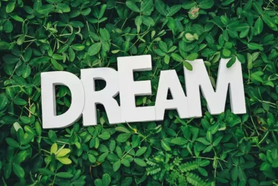 A sign stating Dream, with a background of green leaves