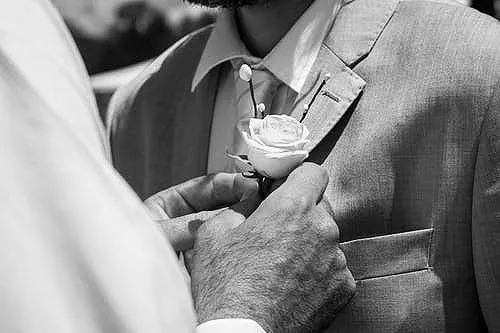 A man pinning a rose to the lapel of another man's jacket