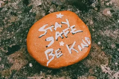 Stay safe and be kind written on a peeble that is painted orange